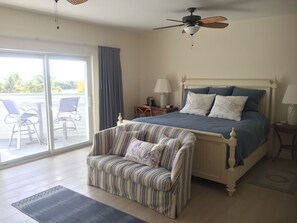 Une chambre à coucher comprenant un lit, une chaise, une table de chevet, une lampe, un ventilateur de plafond et une vue sur l’extérieur.