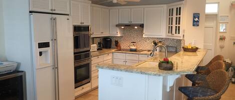 A kitchen with white cabinets, a refrigerator, an oven, a microwave, a sink, and a ceiling fan.