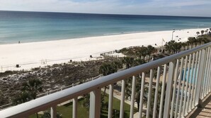 Une vue sur la plage depuis un balcon doté d’une balustrade, avec des palmiers et un ciel dégagé.