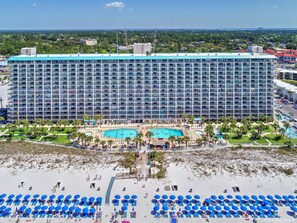 Un grand hôtel à plusieurs étages, doté d’une piscine et d’un accès à une plage avec des chaises longues.