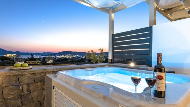 A hot tub with two glasses of red wine and a bottle of wine, overlooking a scenic view of the sea and mountains. - Aelia Suites Milos (Milos)