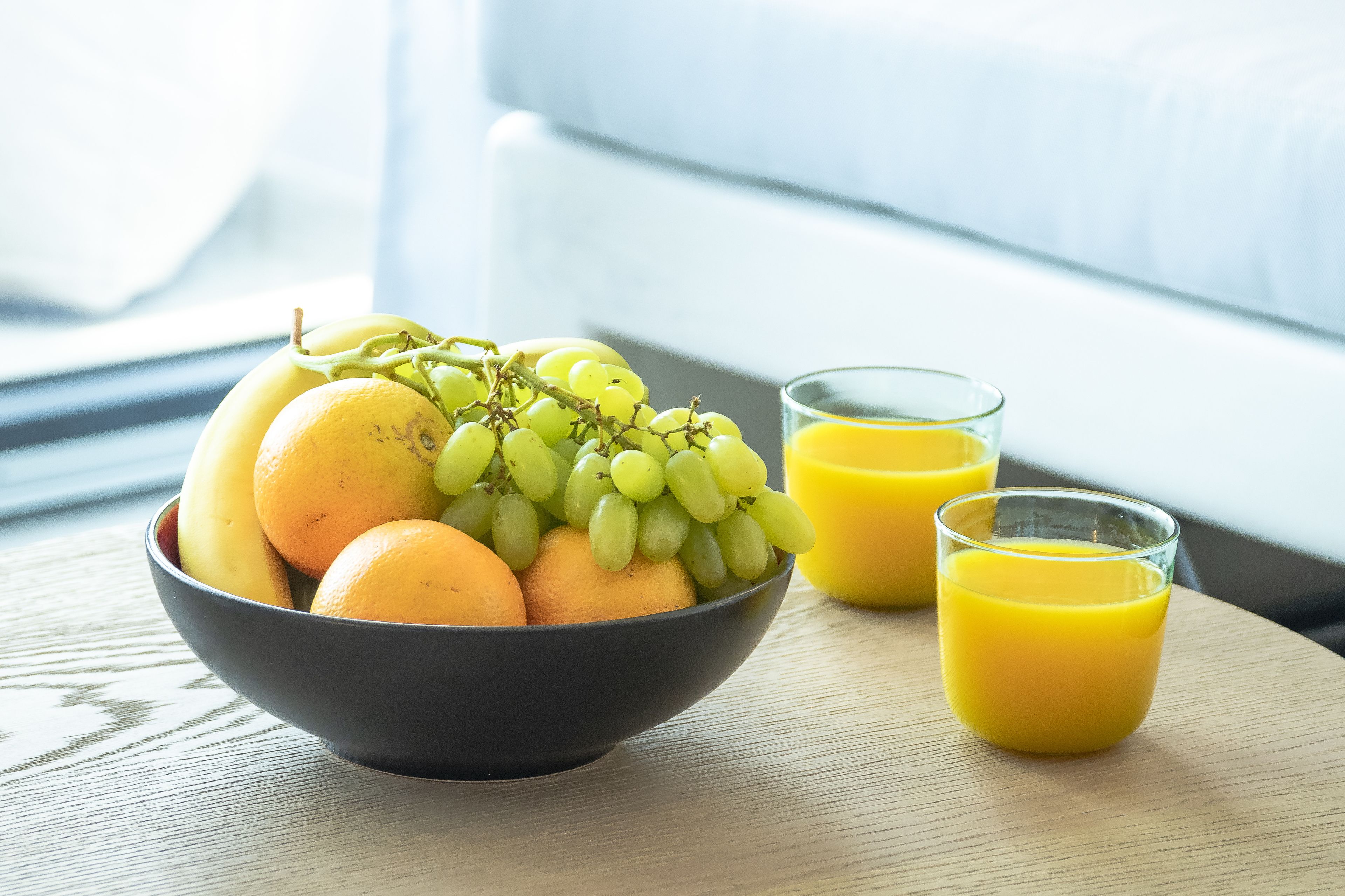 Un bol de fruta y dos vasos de jugo de naranja sobre una mesa de madera.
