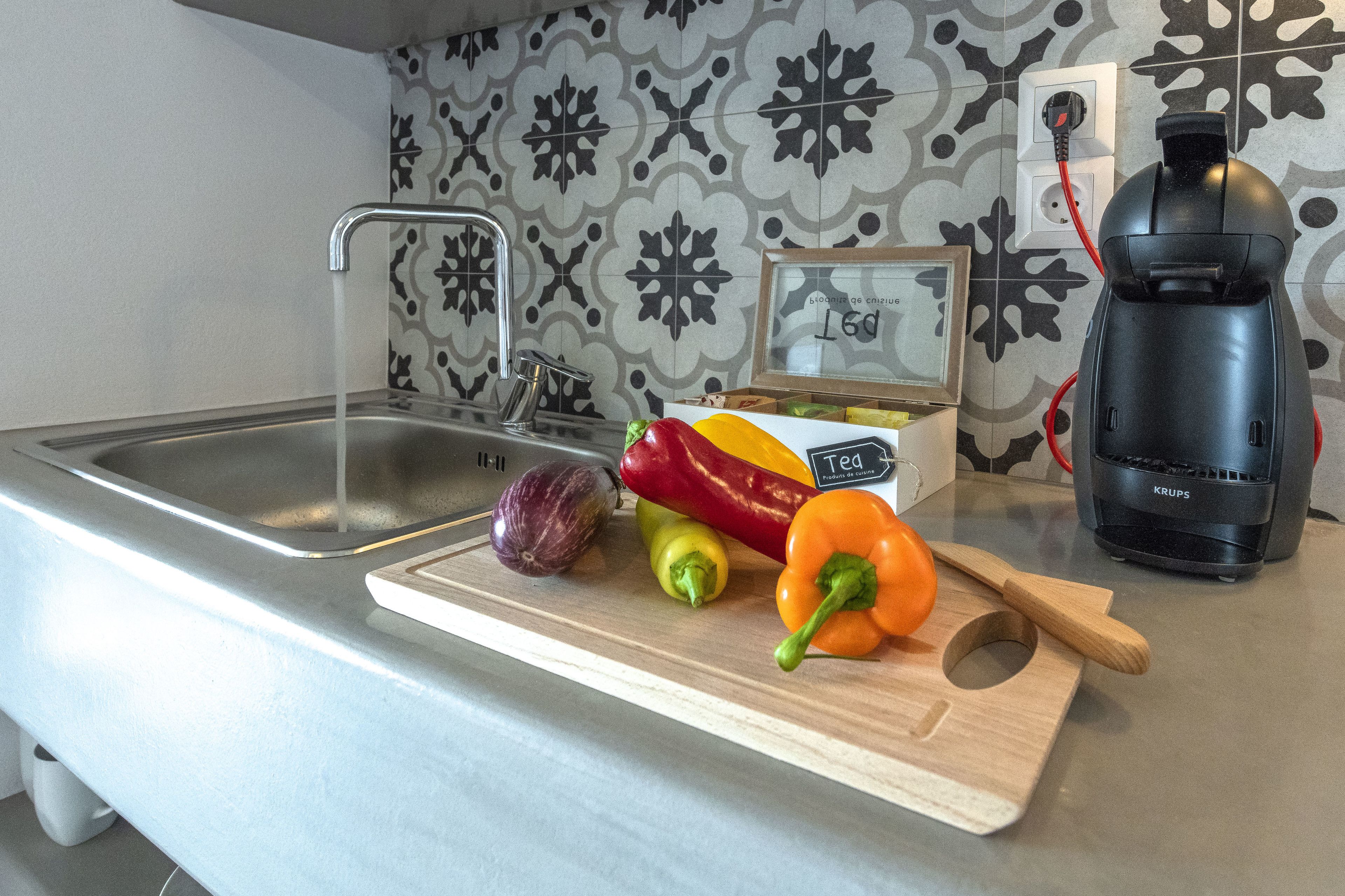 A kitchen counter with a cutting board holding vegetables, a sink, and a coffee maker.