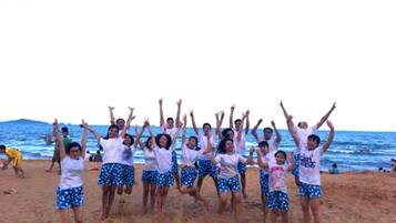 A group of people on a beach with their arms raised, wearing white tops and blue patterned shorts.