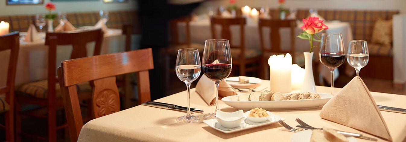 Une table à manger dressée avec des verres à vin, une bougie et une assiette de nourriture.