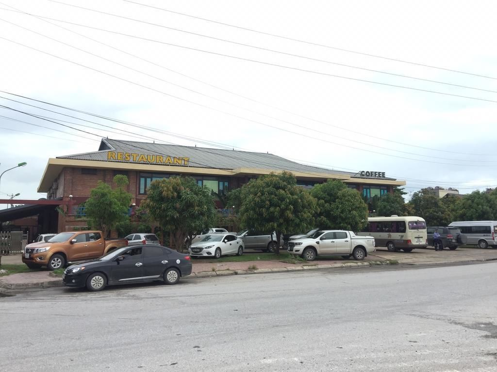 Restaurante com café no andar superior, carros estacionados e um ônibus ao fundo.