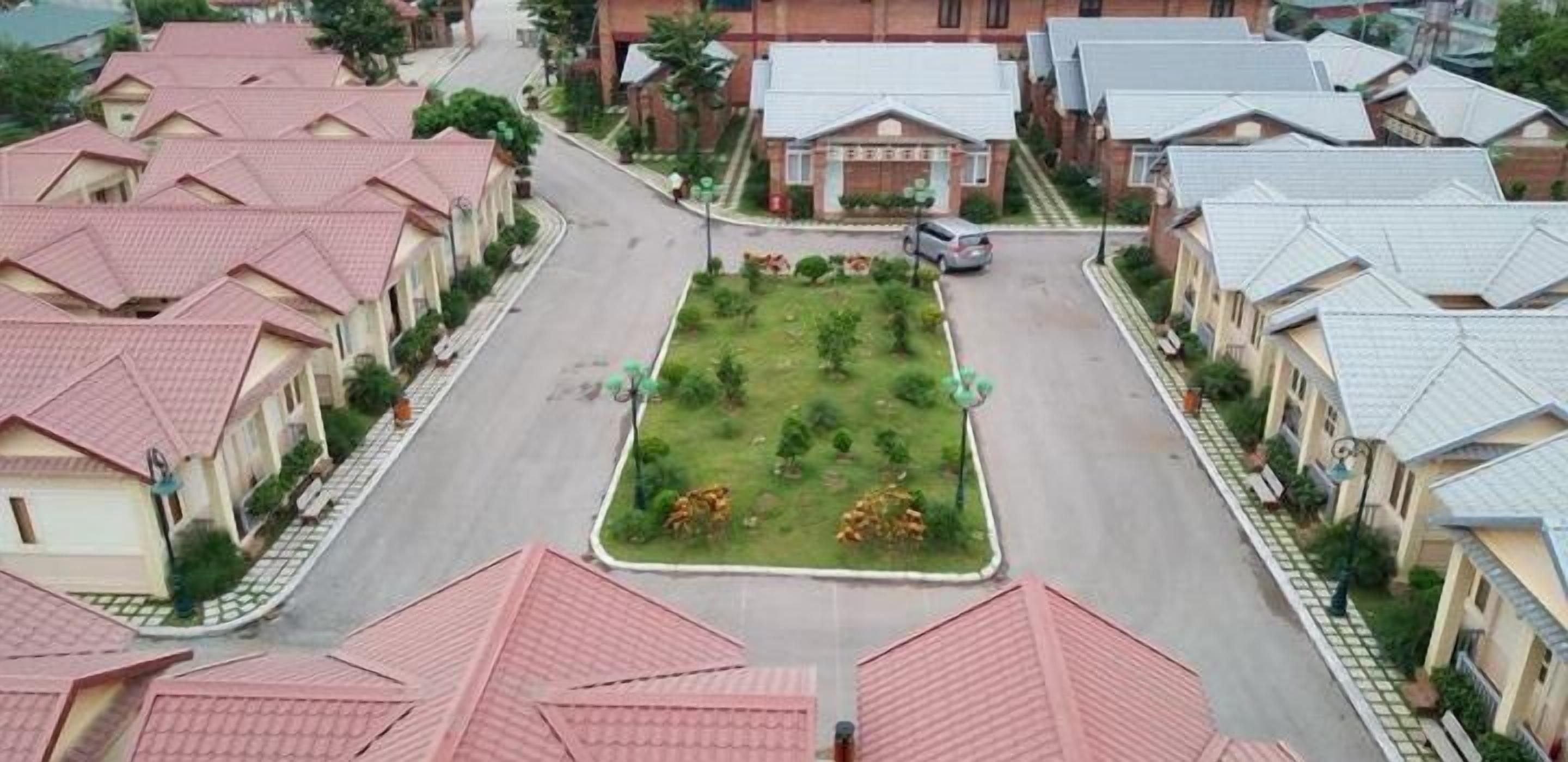 Une rue résidentielle bordée de maisons, avec un espace vert central et une voiture garée.