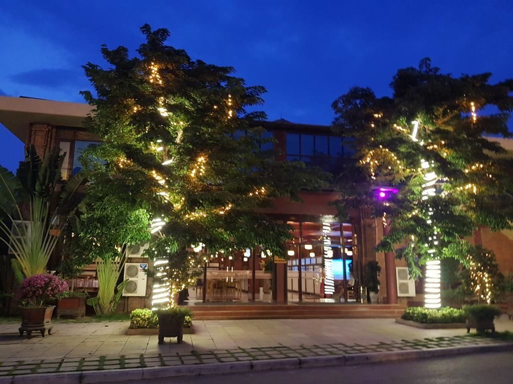 Een hotelentree met een overdekte doorgang, verlichte bomen en een gebouw met grote ramen.