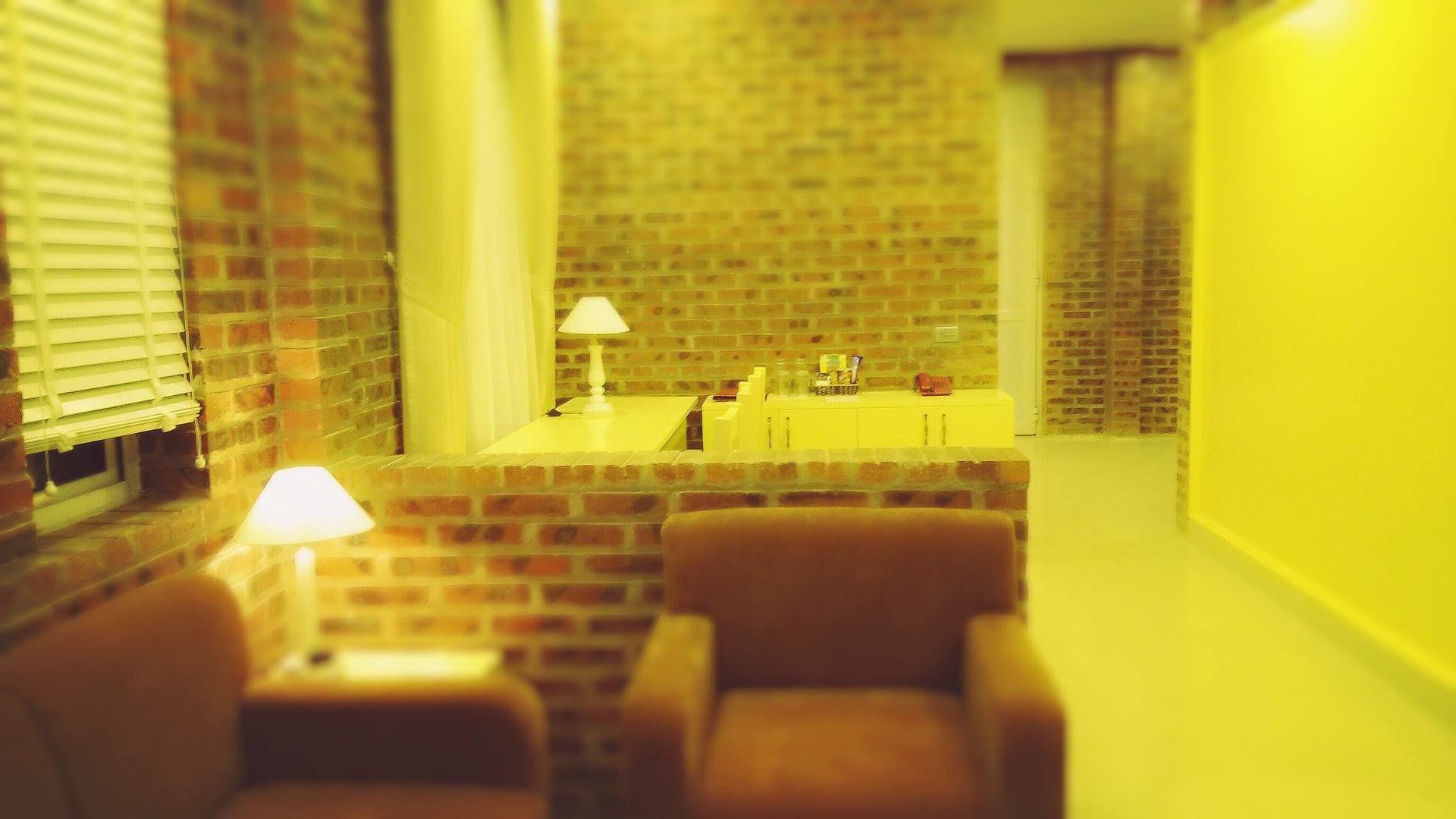 A room with a brick wall, a small table, a chair, and a lamp.