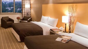 Une chambre d’hôtel avec deux lits, un bureau avec une télévision, une chaise, une lampe et une vue sur la ville.
