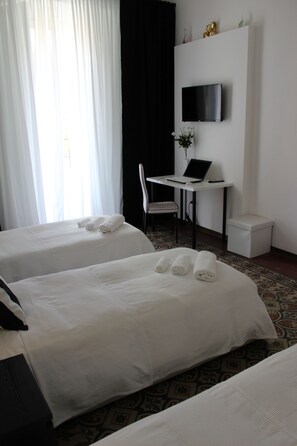 Habitación de hotel con dos camas, un escritorio con una computadora portátil, una silla y un televisor montado en la pared.