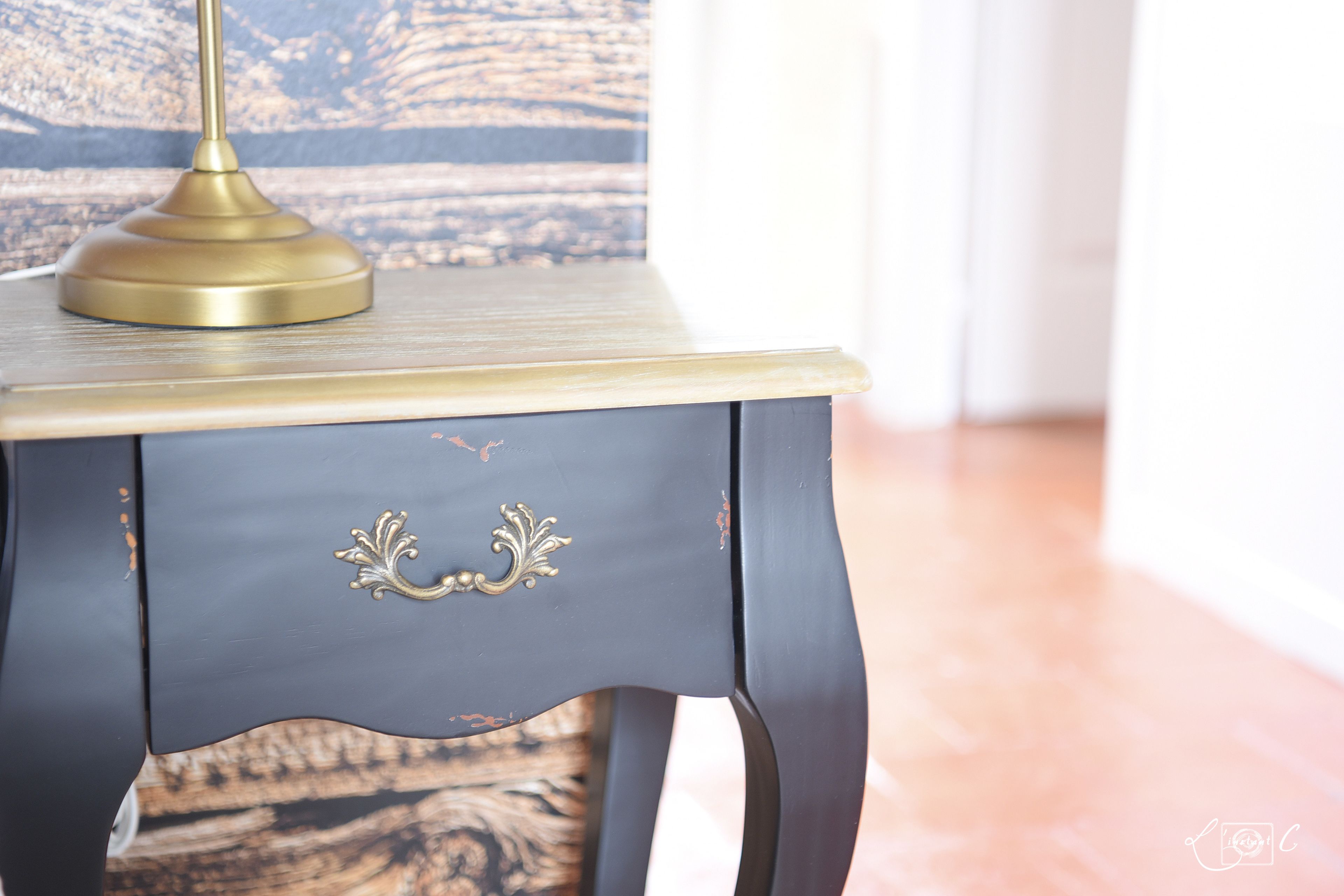 Une table de chevet bleu foncé, ornée d’une lampe en laiton et d’une poignée décorative.