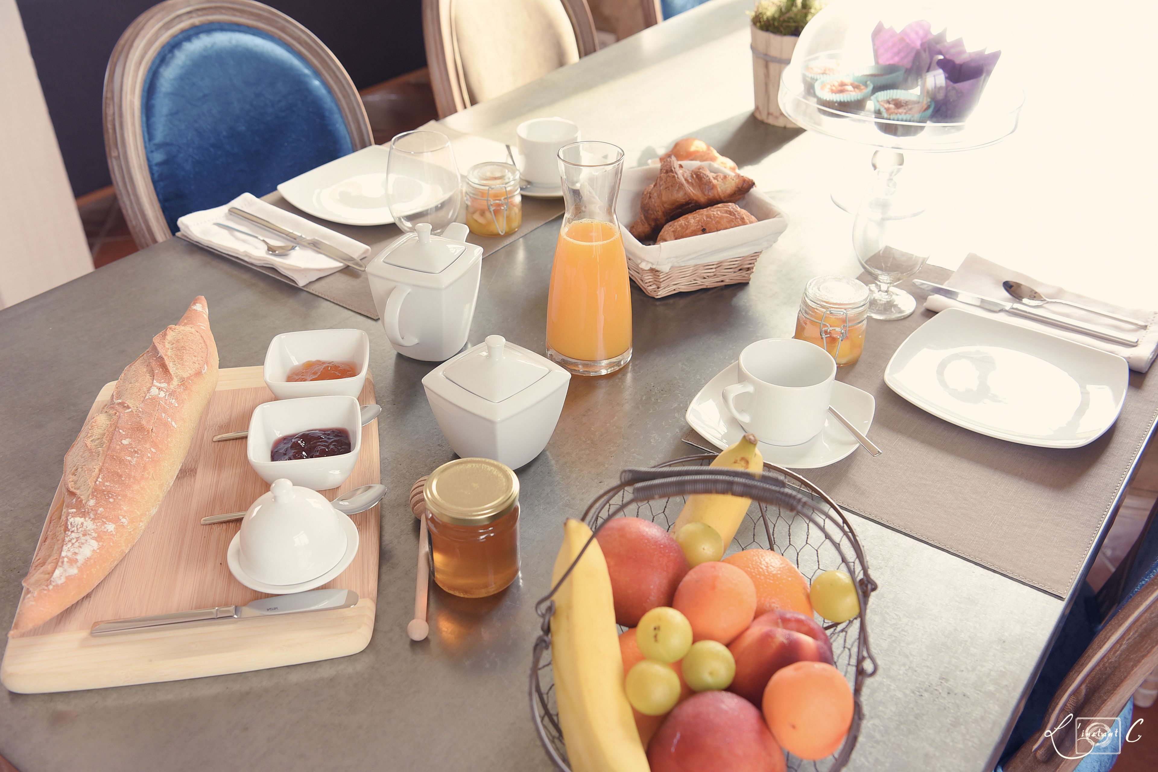 A breakfast table set with croissants, fruit, honey, and coffee.
