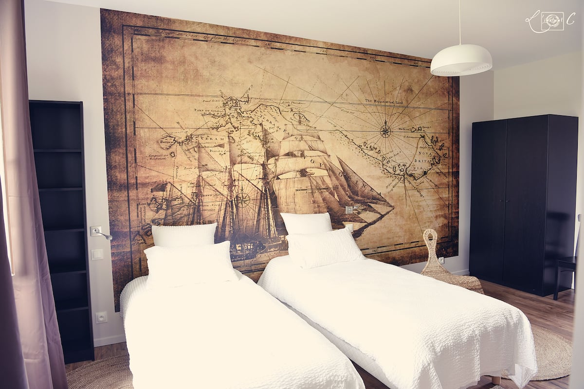 Un dormitorio con dos camas, un mural de un gran mapa en la pared, un armario y una lámpara colgante.