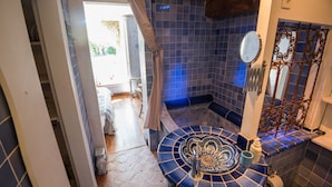 Een badkamer met een blauw betegelde douche, een wastafel met een decoratieve wasbak en een spiegel aan de muur.