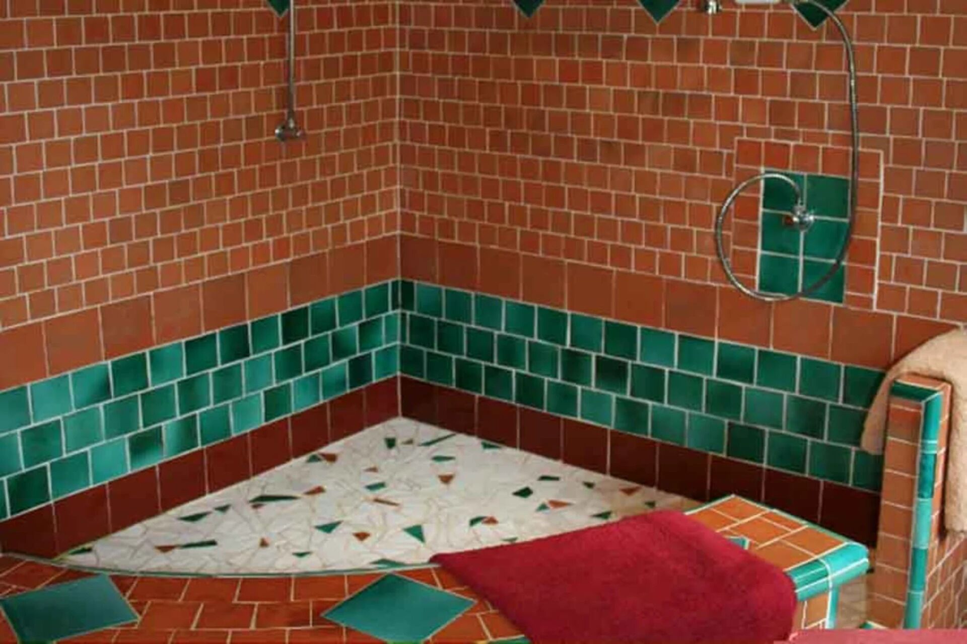 A bathroom with red and green tiled walls, a white patterned floor, and a red towel on the floor.