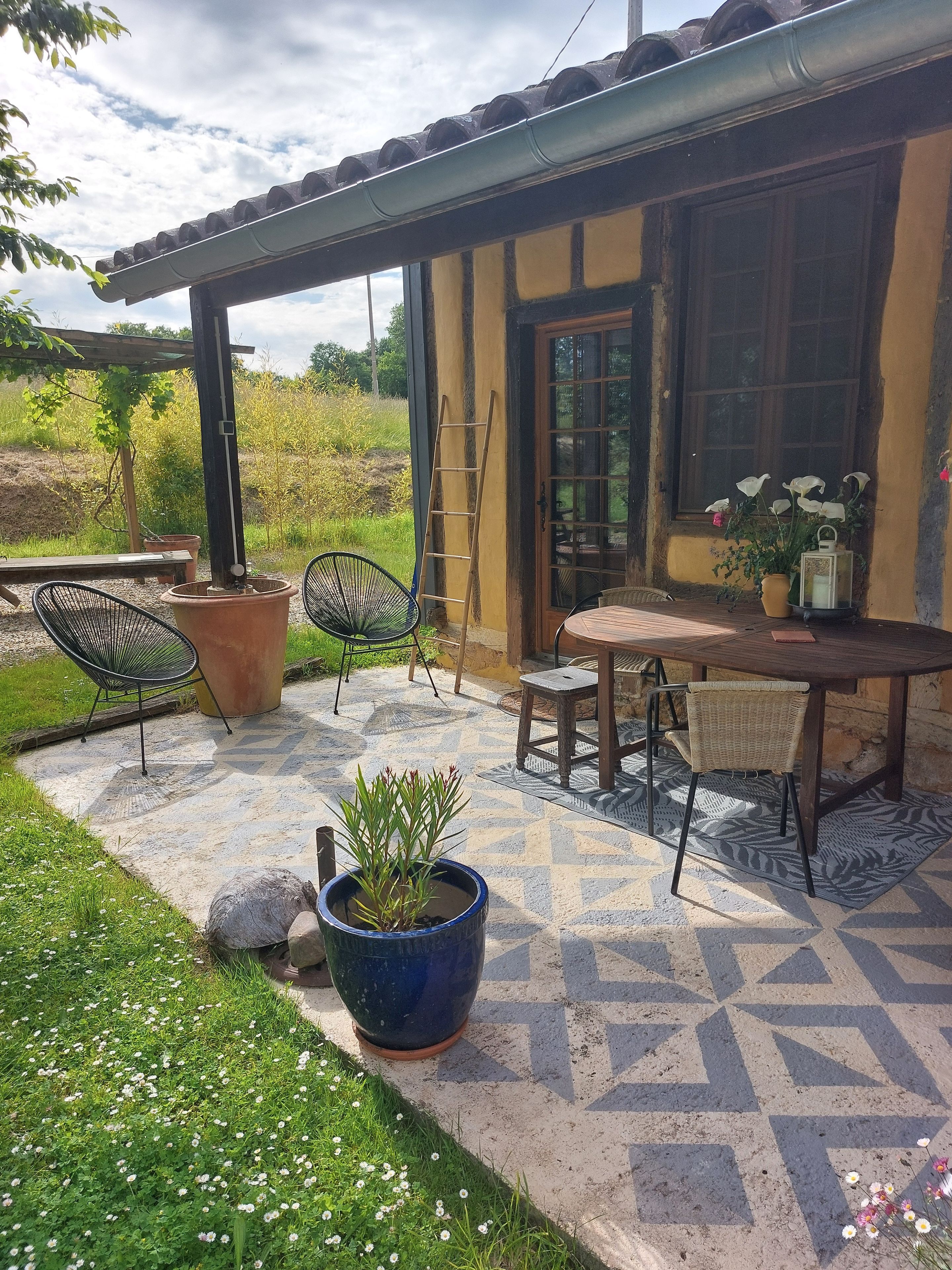 Un espace extérieur aménagé en terrasse, avec une table et des chaises, des plantes en pot et une vue sur le paysage environnant.