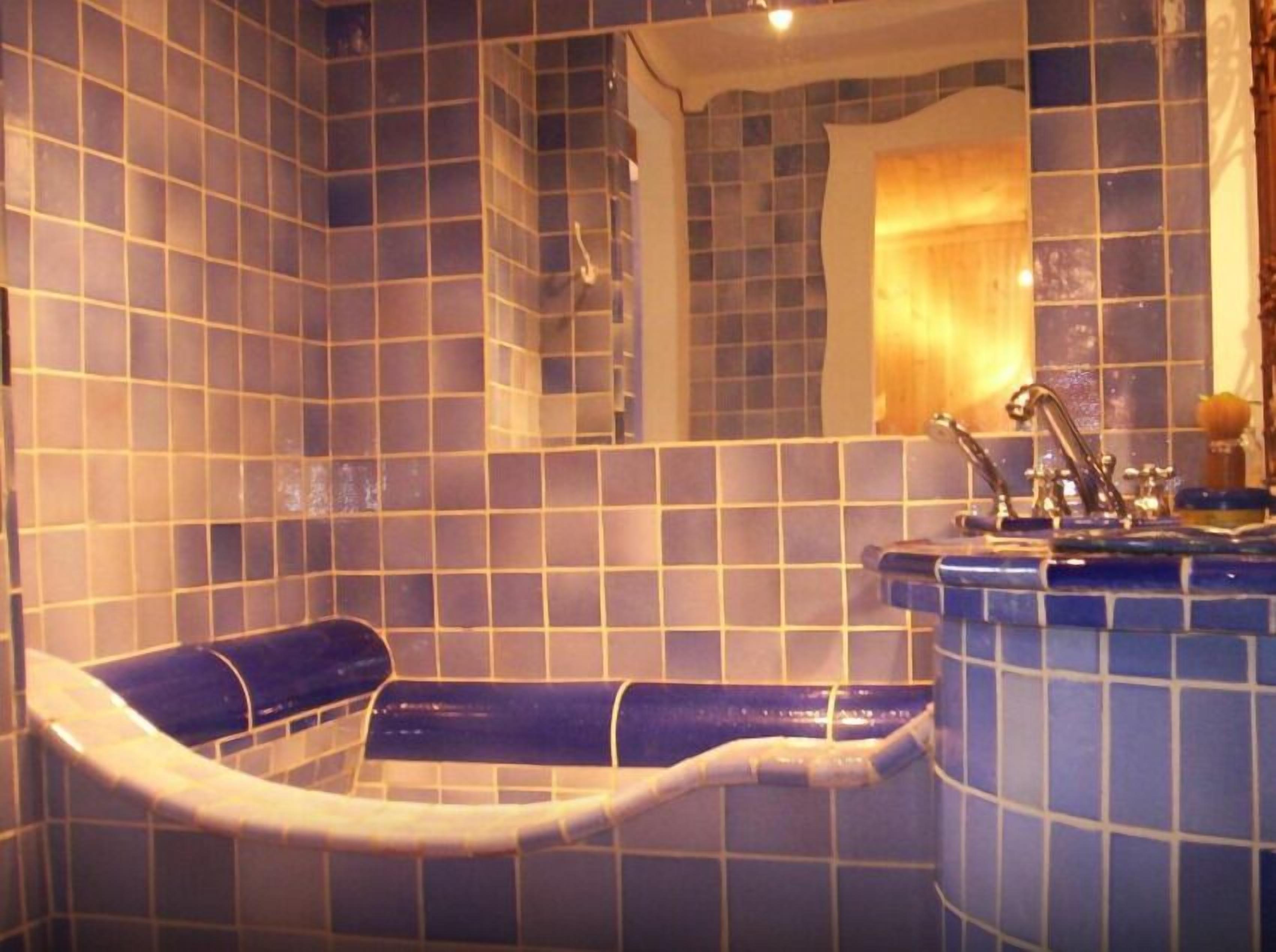 Bany amb parets de rajola blava, una banyera i un lavabo amb un mirall a sobre.