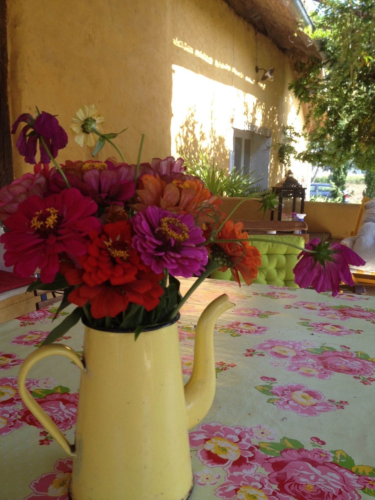 Un vase jaune orné de fleurs, posé sur une table recouverte d’une nappe à motifs floraux.