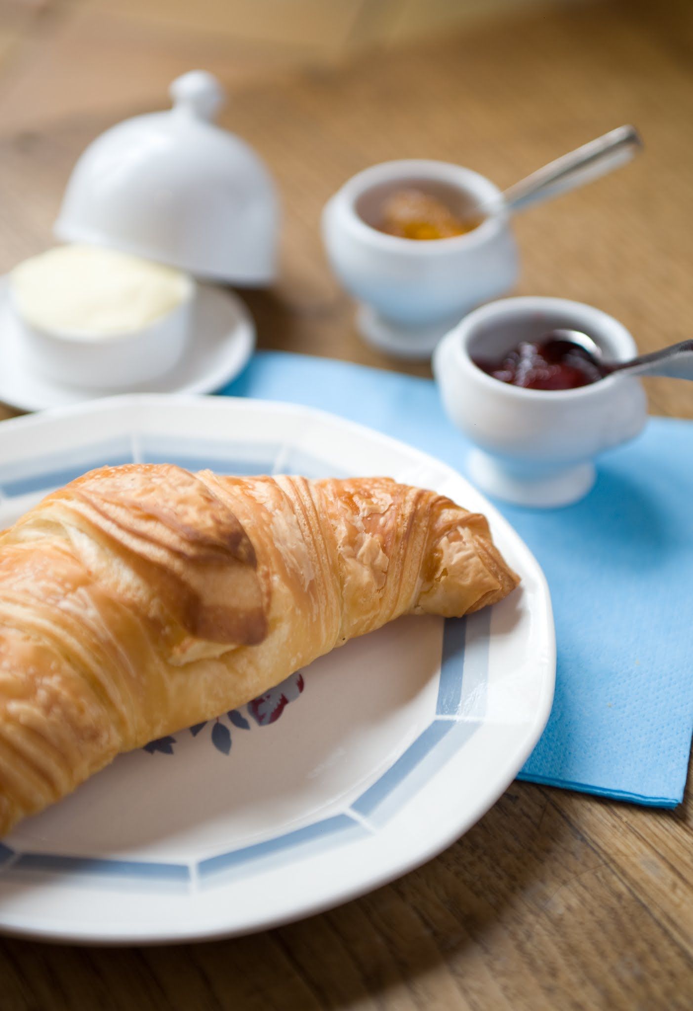 Une assiette avec un croissant et deux petits bols de confiture sur une table en bois.