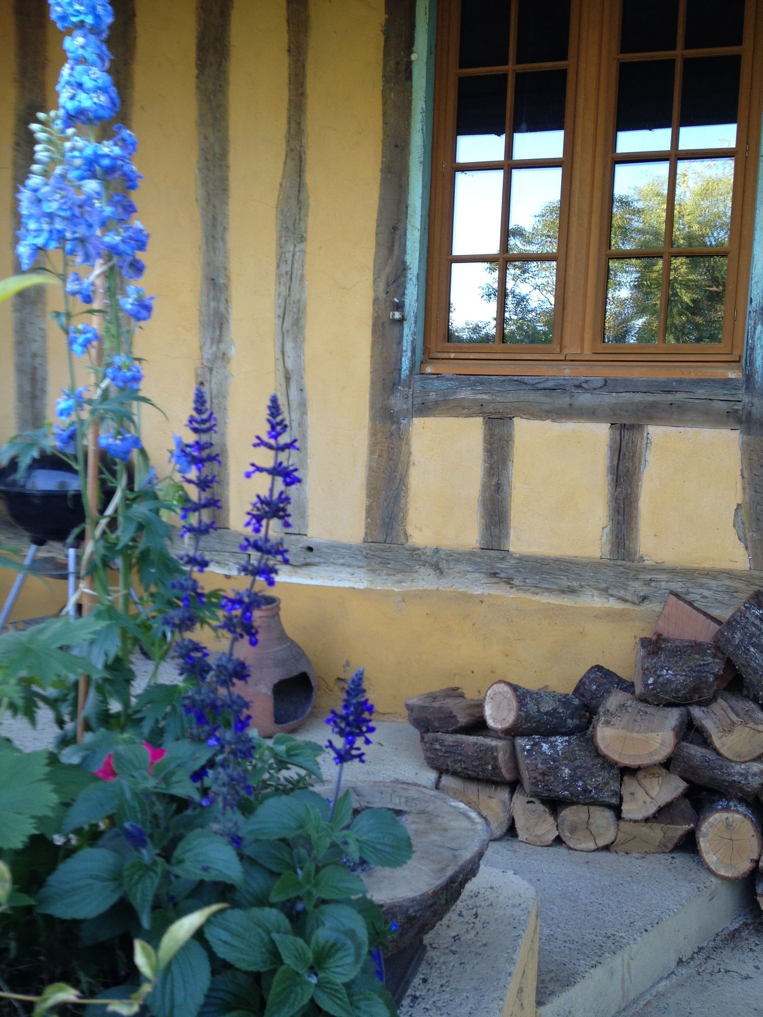 A rustic building with a yellow exterior, a wooden window, and a stack of firewood.