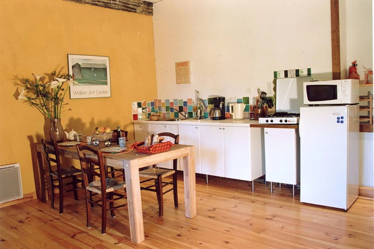 A compact kitchen with a dining area, featuring a wooden table, chairs, a microwave, and a small refrigerator.