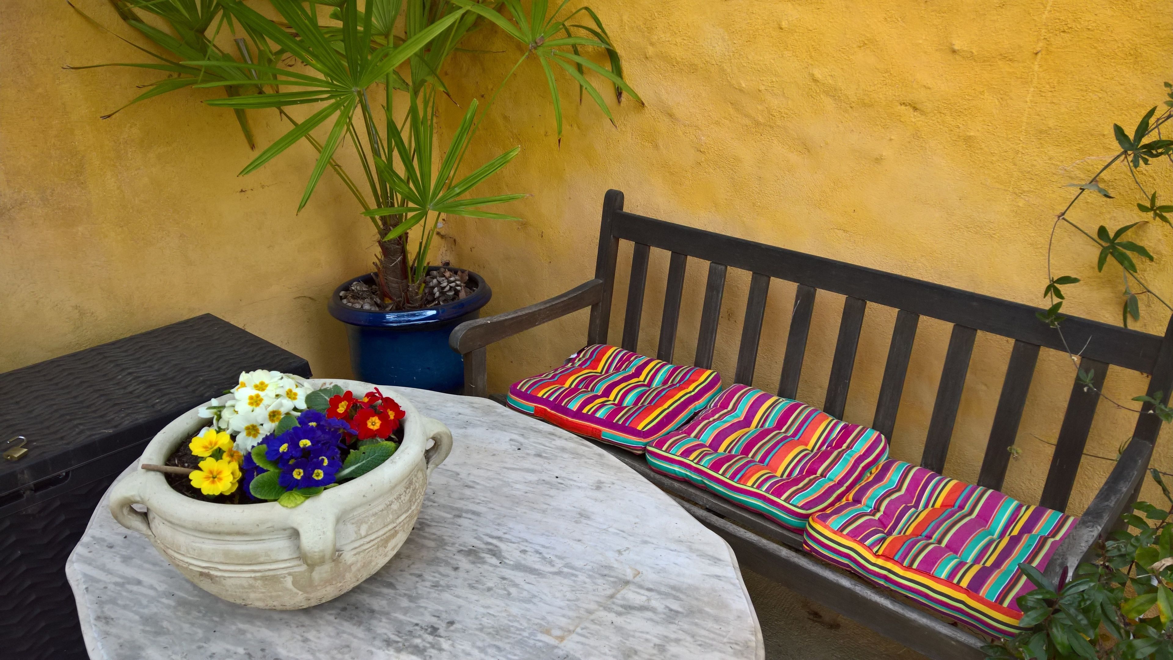 A small outdoor seating area with a bench and a table, a potted plant, and a flower pot on the table.