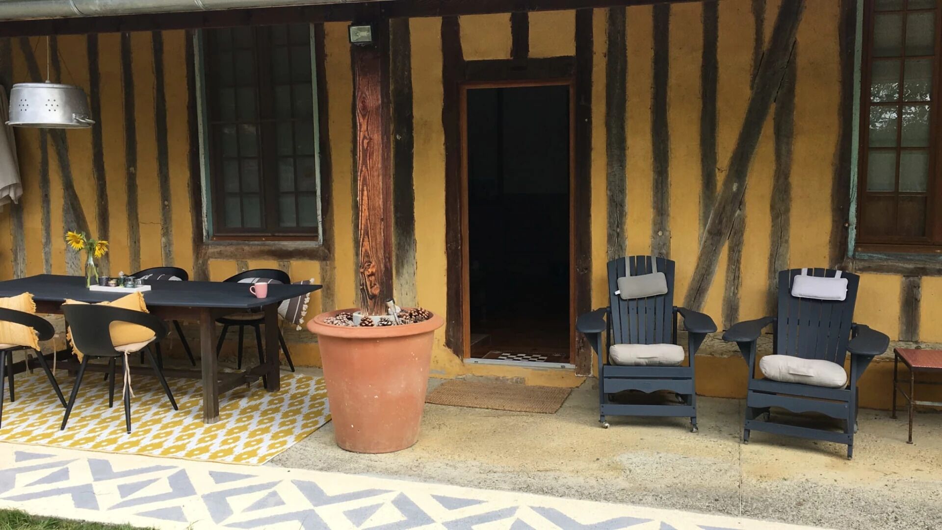 An outdoor seating area with a table and chairs, a large terracotta pot, and a wooden door.