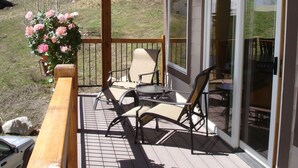 Een overdekt terras met stoelen en een tafel, met uitzicht op een glooiend grasveld.