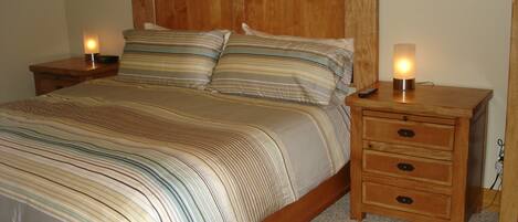 A wooden bed with striped bedding, two bedside tables with lamps, and a carpeted floor.
