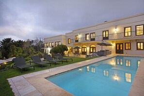 Une piscine avec des chaises longues et un bâtiment bien éclairé en arrière-plan.
