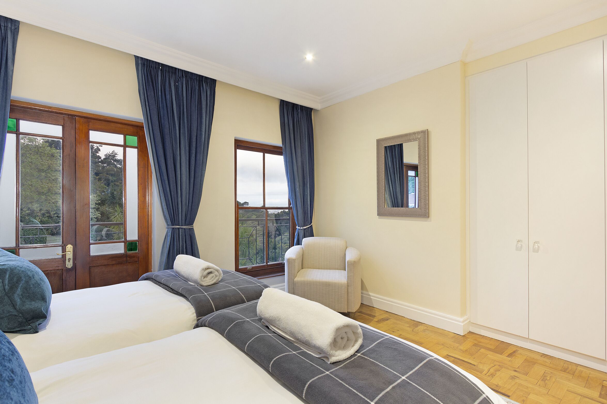A hotel room with two beds, a chair, a wardrobe, and a balcony with curtains.