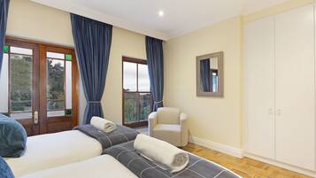 A hotel room with two beds, a chair, a wardrobe, and a balcony with curtains.