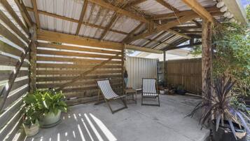 A covered patio with two striped lounge chairs, potted plants, and a wooden fence in the background.