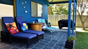 A covered patio with two blue cushioned chairs, a small round table, and a barbecue grill. - 3 Min walk to the beach,  this little slice of heaven is your perfect getaway! (Culburra Beach)