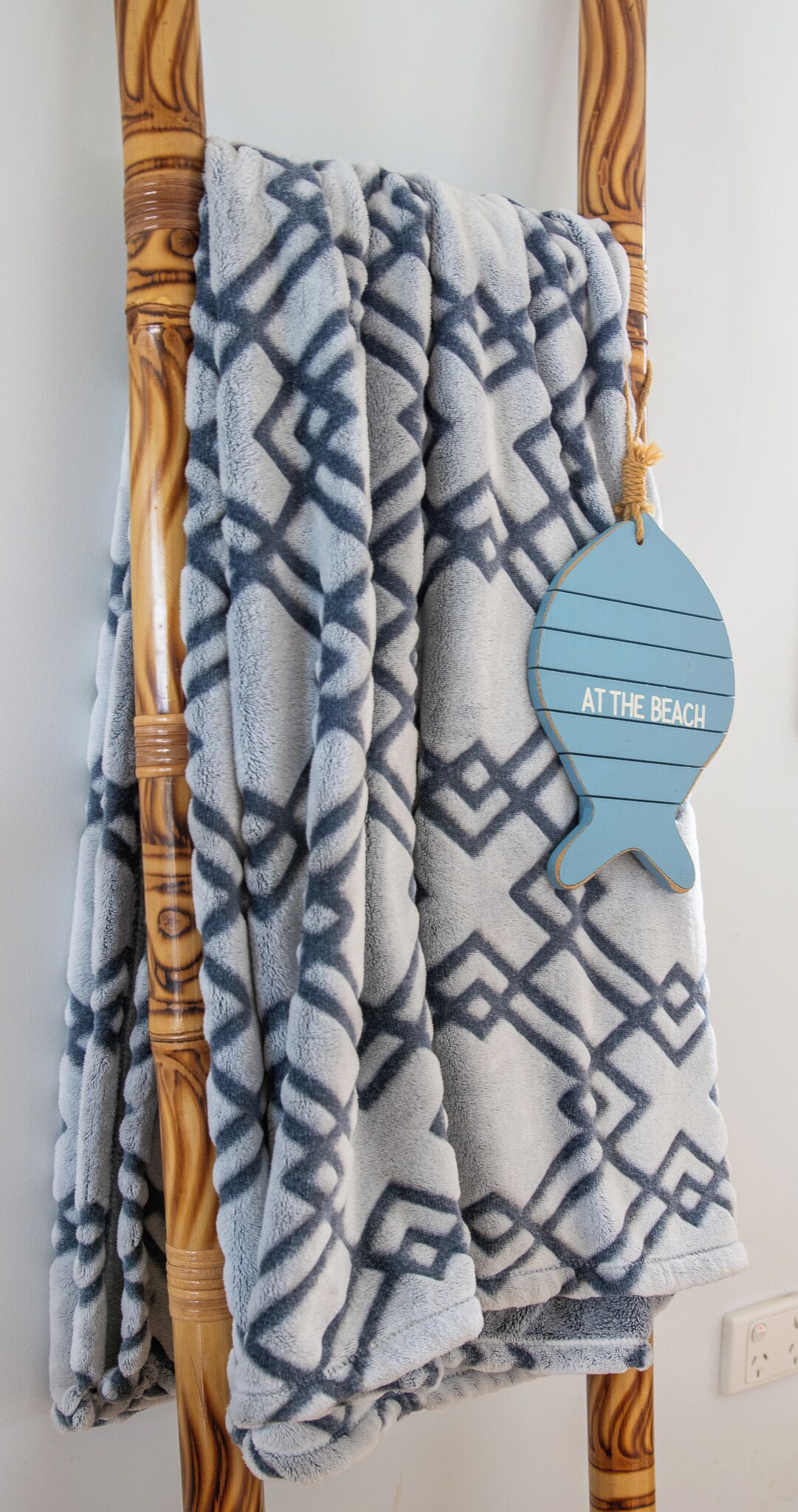 A patterned towel hanging on a wooden towel rack with a decorative sign that reads 'AT THE BEACH'.