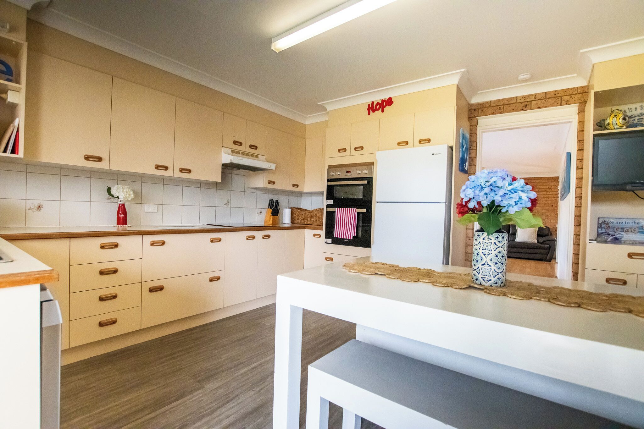 Une cuisine moderne avec des meubles en bois clair, un plan de travail blanc et un four encastré.