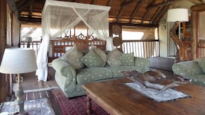 A room with a thatched roof, a green sofa with patterned cushions, a wooden coffee table, and a traditional lamp. - Treetops Holiday Home (Nkomazi)