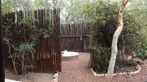 A fenced garden area with a gravel path, a circular concrete structure, and a tree. - Treetops Holiday Home (Nkomazi)