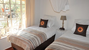A room with two beds, each with striped bedding and decorative pillows. There is a window with curtains, a bedside table with a lamp, and a mosquito net above the beds. - Treetops Holiday Home (Nkomazi)