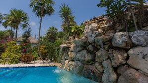Une piscine à l’eau d’un bleu limpide, entourée de plantes tropicales et bordée d’un mur de pierre.