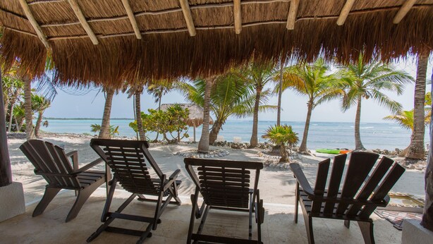 Une terrasse au bord de la plage, dotée d’un toit de chaume, de trois fauteuils Adirondack et offrant une vue sur l’océan.