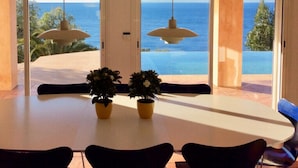 A dining area with a table and chairs, potted plants, and a view of the ocean through glass doors. - Residential villa with big swimming-pool in Antheor, Southern France (Saint-Raphaël)
