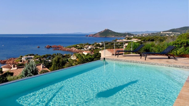 A clear blue swimming pool with lounge chairs and a view of the sea and hills. - Residential villa with big swimming-pool in Antheor, Southern France (Saint-Raphaël)