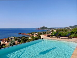 A clear blue swimming pool with lounge chairs and a view of the sea and hills. - Residential villa with big swimming-pool in Antheor, Southern France (Saint-Raphaël)