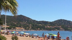 A beach with people sunbathing and swimming, palm trees, and a hilly background. - Residential villa with big swimming-pool in Antheor, Southern France (Saint-Raphaël)