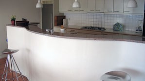 A modern kitchen with a curved island, white cabinets, pendant lighting, and a coffee maker. - Residential villa with big swimming-pool in Antheor, Southern France (Saint-Raphaël)