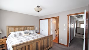 Een slaapkamer met een houten bed, een nachtkastje, een lamp en een deur naar een andere kamer.