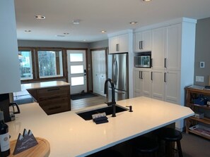 A modern kitchen with white cabinetry, a stainless steel refrigerator, and a large island with a sink.