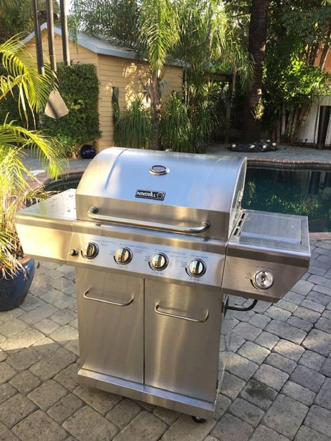 Ein edelstahlfarbener Outdoor-Grill mit vier Kochfeldern, einem Seitenbrenner und integriertem Thermometer.
